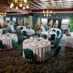 Large dining room with green chairs and white rounded tables for wedding events
