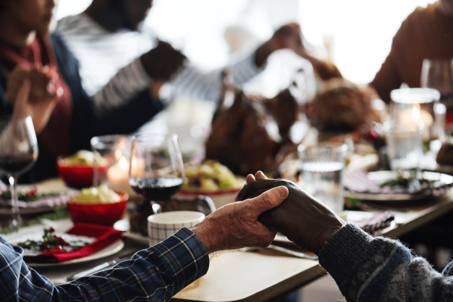 family gathered around table holding hands for prayer before thanksgiving dinner