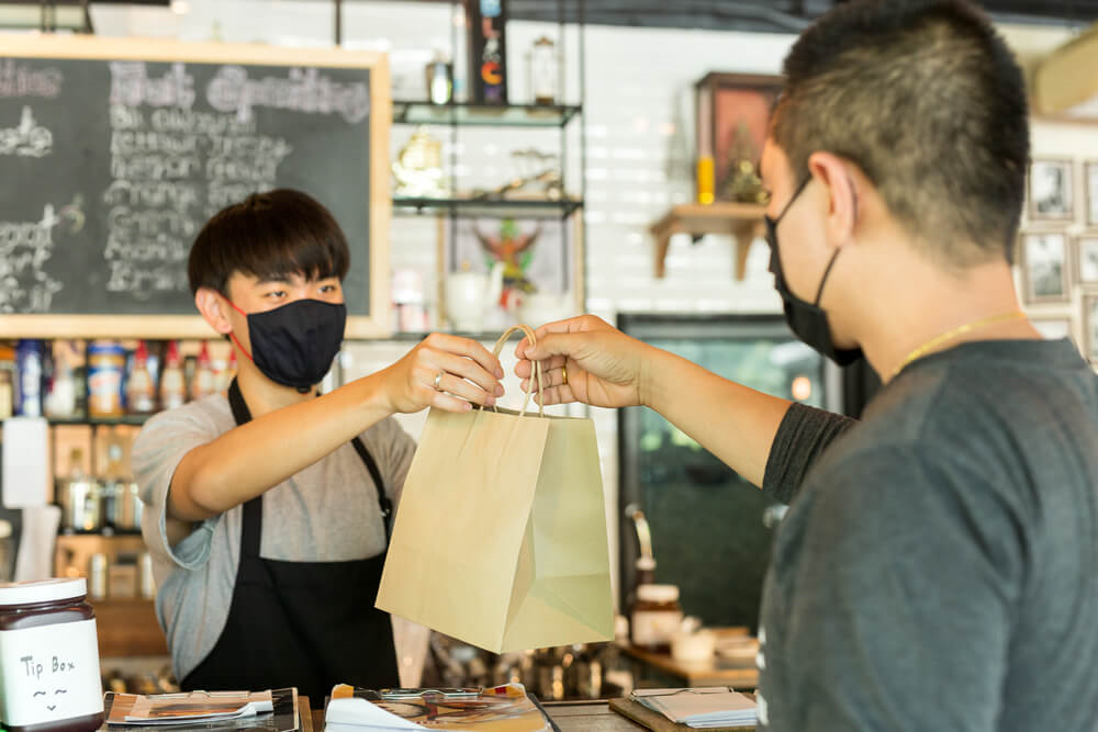 A man, wearing a mask, grabs a takeout bag from a cashier, also wearing a mask, at one of the many Rehoboth Beach restaurants.