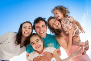 family of couple and three kids smiling with a sky colored background